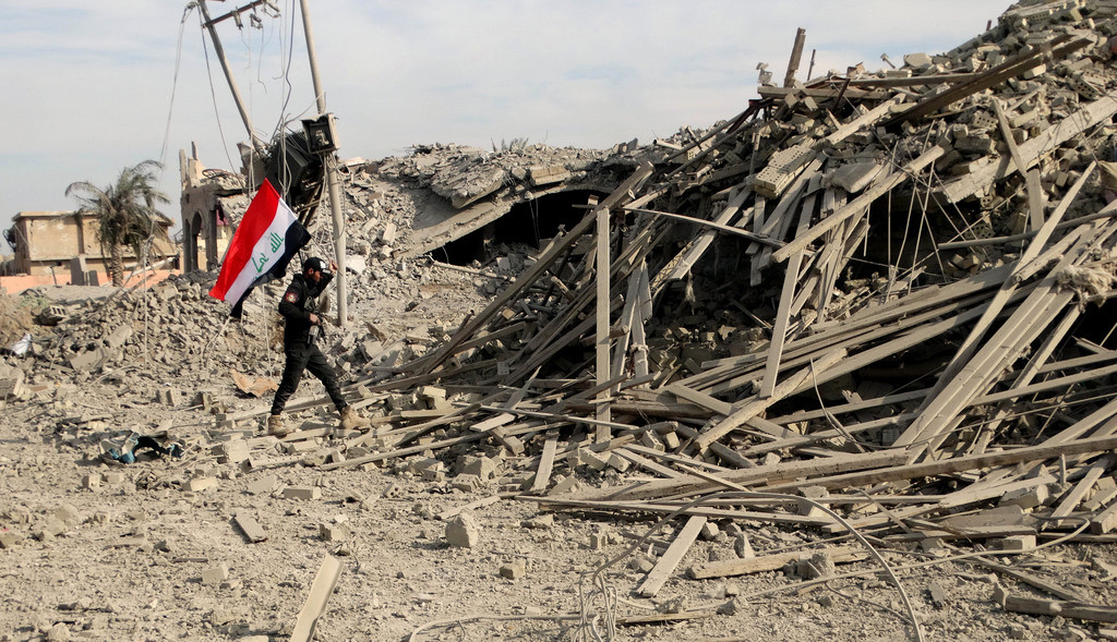 Ramadi, 115 Kilometer westlich von Bagdad, am 27. Dezember: Ein Soldat der irakischen Armee mit der Nationalflagge erreicht das zerstörte Gebäude der Provinzverwaltung im Zentrum der Stadt. Der „Islamische Staat“ erleidet eine wichtige Niederlage. (Foto: Keystone/AP, Osama Sami)
