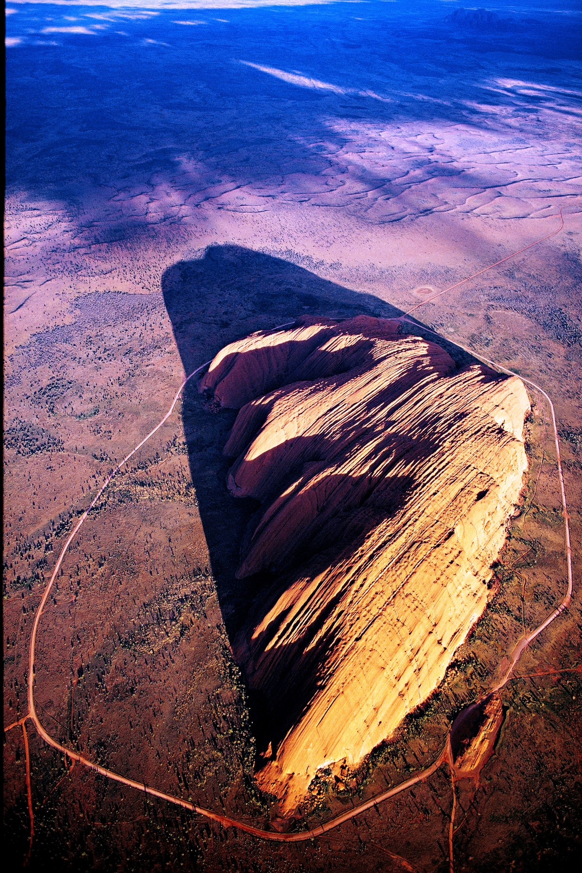 Der Uluru, 348 Meter über die umgebende Wüste emporragend, ist ein Berg der dritten Art: ganz eingesponnen in die „Traumzeit“ der örtlichen Ureinwohner.
Mag ja sein, dass der Fels im roten toten Herzen Australiens schon kraft seiner Natur weltweit einzigartig ist – mitnichten ist er aber ein Monolith, obwohl sogar die Unesco dieses Touristenlatein nachplappert. Und als Inselberg aus geschichtetem Sandstein, den Erosion und Verwitterung aus einer Rumpffläche herauspräparierten, ist er nicht einmal – so ein…