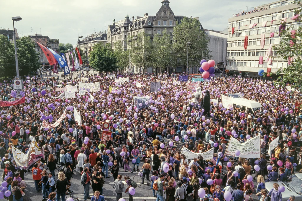 14. Juni 1991: Frauenstreik in der Schweiz: Im ganzen Land legt eine halbe Millione Frauen die Arbeit für einige Stunden oder den ganzen Tag nieder. Überall finden Kundgebungen statt. Allein auf dem Helvetiaplatz in Zürich (Bild) versammeln sich Tausende. Sie fordern die Umsetzung des vor zehn Jahren in Kraft getretenen Verfassungsartikels über die Gleichstellung von Mann und Frau. Die Frauen kritisieren, dass zehn Jahre nach Inkrafttreten des Gleichstellungsartikels von Gleichstellung, vor allem in finanz…