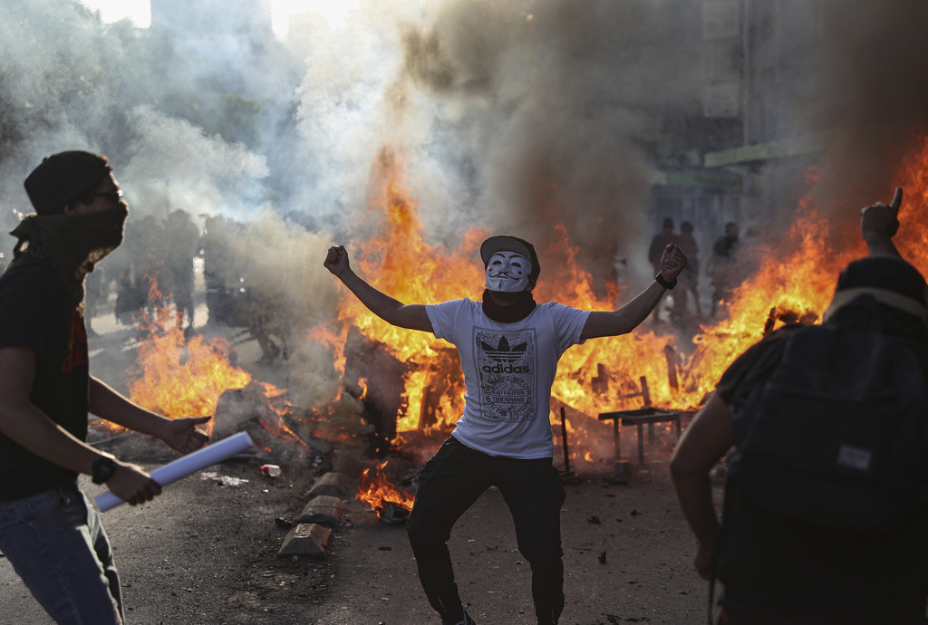 A demonstrator wearing a mask dances in front of a burning barricade during a protest in Santiago, Chile, Thursday, Nov. 28, 2019. It's been weeks since the most potent civil unrest in Chile's recent history broke out. Most of the demonstrators are peaceful but a much smaller group of masked protesters has used street violence, wreaking havoc in many cities. Twenty-six people have died and thousands more have been injured. (AP Photo/Esteban Felix) 