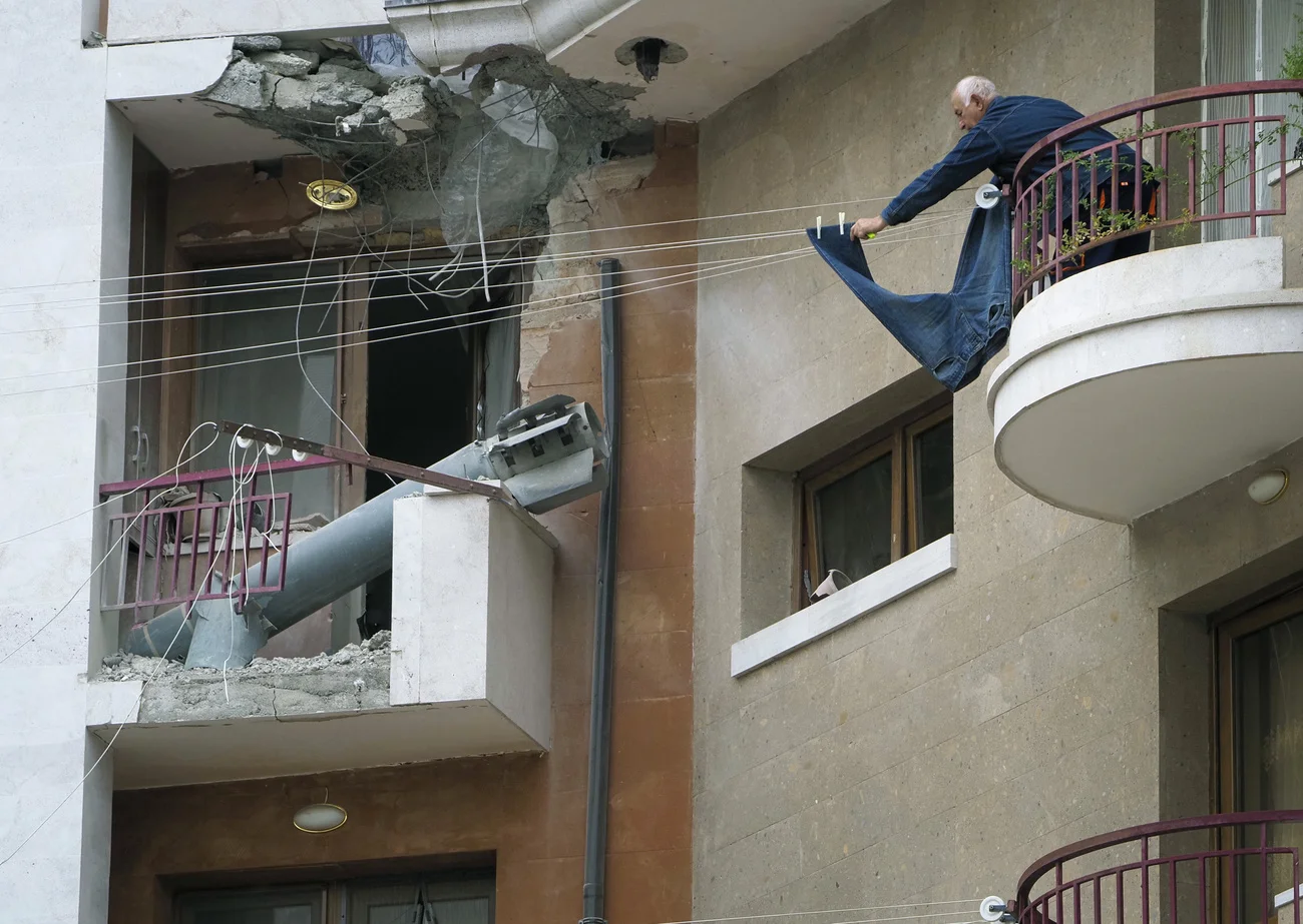 Das Bild vom Samstag stammt aus Stepanakert, dem Hauptort von Nagorno Karabakh. Es zeigt eine aserbaidschanische Polonez-Rakete nach ihrem Einschlag in ein Wohnhaus. Daneben hängt ein Mann ein Paar Jeans an eine Wäscheleine. (Foto: Keystone/AP)
