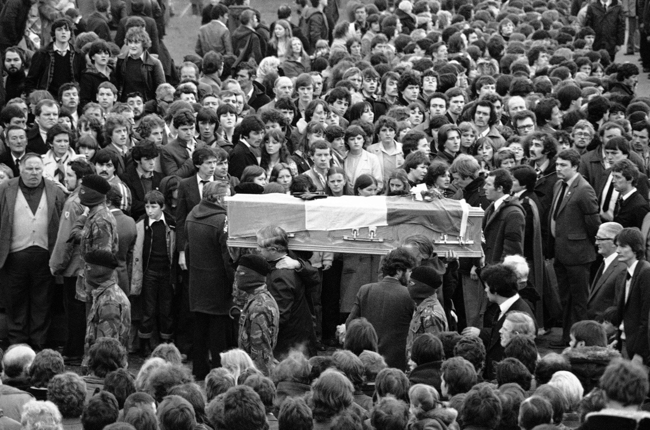 In einem nordirischen Gefängnis stirbt der IRA-Aktivist Bobby Sands. Er hatte sich 66 Tage im Hungerstreik befunden. Es kommt zu schweren Ausschreitungen. An der Beerdigung in Belfast nehmen hunderttausend Menschen teil. Maskierte IRA-Aktivisten begleiten den Sarg. (Foto: Keystone/AP/Peter Kemp)