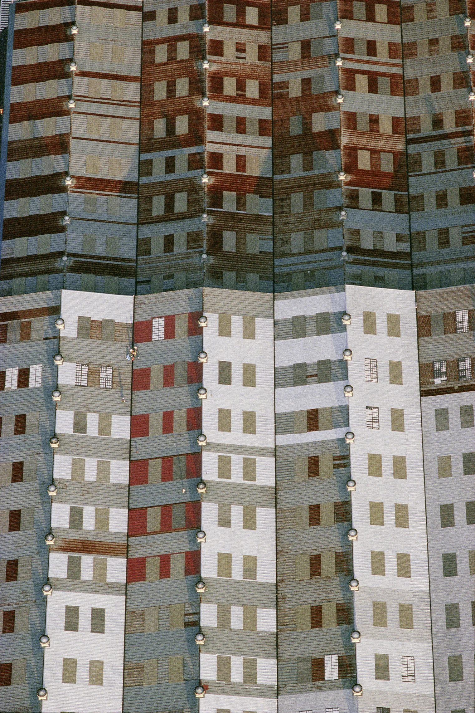 Dach einer Werkhalle in Yokohama, Japan 1982. Der Augenschein täuscht: nicht Ansicht ist Sache, sondern Aufsicht. Nicht die Fassade eines Hochhauses, sondern der Ausschnitt eines Industriedachs. Für Farbe sorgt der Anstrich, der das Blechdach vor Korrosion schützt. Ventilatoren auf den Dachfirsten für Belüftung und Entlüftung sowie durchscheinende Paneele, die Tageslichtflächen im Dach, sind weitere graphische Bildelemente,

(Copyright Georg Gerster/Keystone)

http://www.georggerster.com/