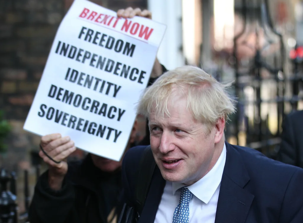 Boris Johnson entscheidet die Urwahl der Konservativen für den Parteivorsitz für sich. Bei der Ankunft bei seinem Büro steht er im Schatten des Plakats eines Brexit-Befürworters. (Keystone/PA via AP, Yui Mok)