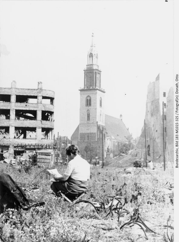 Die ersten Nachkriegstage: Eine Frau sitzt in Berlim auf einem Klappstuhl inmitten von Trümmern und liest. Im Hintergrund die Marienkirche (Bild: DEutsches Bundesarchiv, 183-M1015-325, 1945, Otto Donath)
