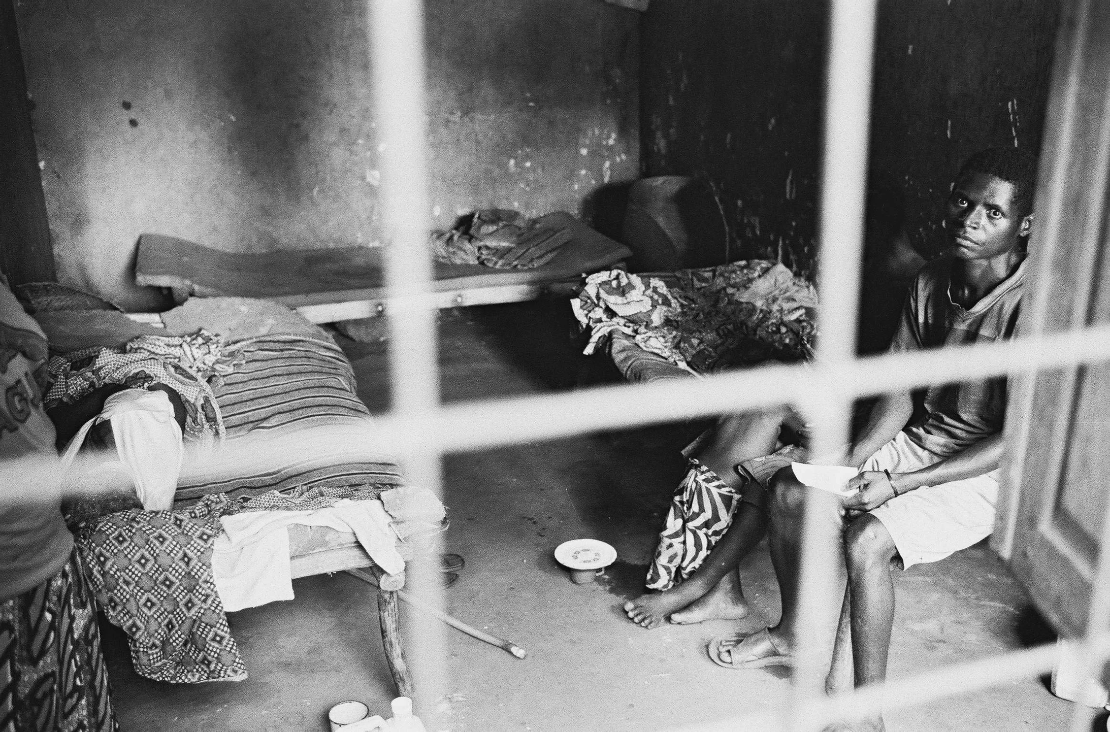 Was wie ein Gefängnis aussieht, ist ein Spital. Angst in den Augen des Mannes, links liegt seine verletzte Frau.