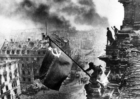 Um die Entstehung des Fotos kreisen zahlreiche Mythen. Bereits vor der Aufnahme dieses Bildes sollen sowjetische Flaggen auf dem Reichstag gehisst worden sein. Sicher ist, dass das berühmt gewordene Bild nachgestellt und erst am 2. Mai entstand. Nicht restlos geklärt ist, wieweit es retouchiert worden ist. Der Rauch im Hintergrund wurde offenbar schwarz eingefärbt, um die Szene zu dramatisieren. (Bild: mil.ru, минобороны.рф), Verteidigungsministeriums der Russischen Föderation)


