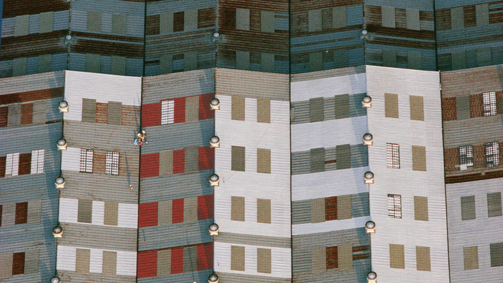 Dach einer Werkhalle in Yokohama, Japan 1982. Der Augenschein täuscht: nicht Ansicht ist Sache, sondern Aufsicht. Nicht die Fassade eines Hochhauses, sondern der Ausschnitt eines Industriedachs. Für Farbe sorgt der Anstrich, der das Blechdach vor Korrosion schützt. Ventilatoren auf den Dachfirsten für Belüftung und Entlüftung sowie durchscheinende Paneele, die Tageslichtflächen im Dach, sind weitere graphische Bildelemente,

(Copyright Georg Gerster/Keystone)

http://www.georggerster.com/