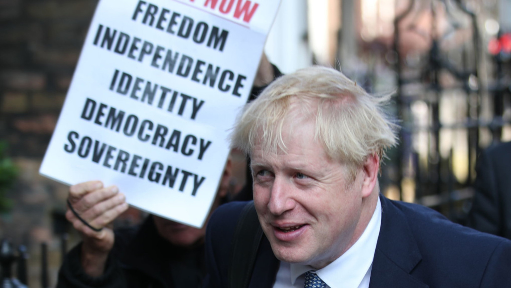 Boris Johnson entscheidet die Urwahl der Konservativen für den Parteivorsitz für sich. Bei der Ankunft bei seinem Büro steht er im Schatten des Plakats eines Brexit-Befürworters. (Keystone/PA via AP, Yui Mok)
